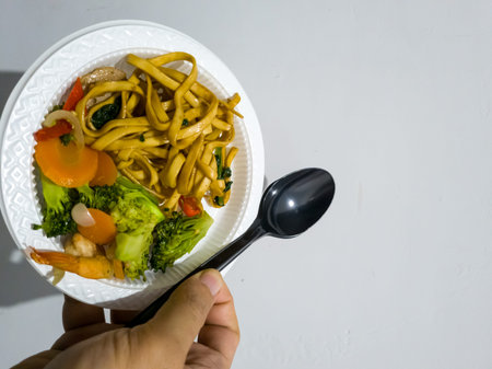 Fried noodles in a white plate with sliced â€‹â€‹toppings and green vegetables
