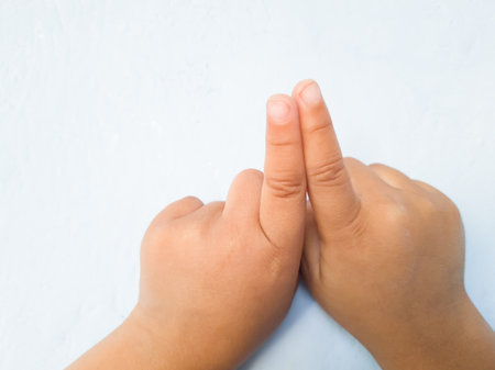 Child's hands making a heart shape on a white wall background.の写真素材