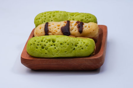 Green tea eclairs on a wooden plate on white background.