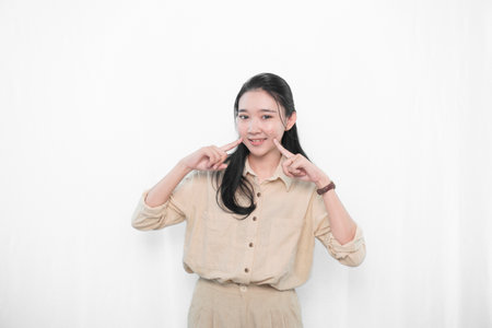 The expression of an Asian model woman in white clothes smiling and putting her index finger to her cheekの写真素材