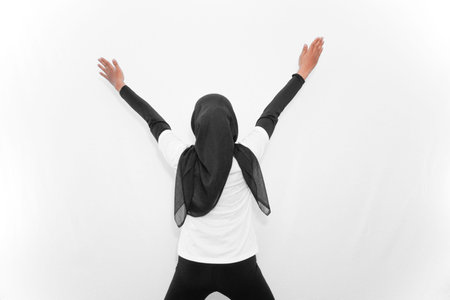 A woman does gymnastics, facing backwards with two hands above her head.