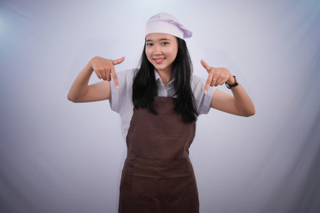 Asian Indonesian woman wearing chef's uniform smiling and pointing downの写真素材