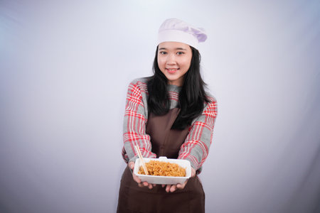 Indonesian Asian woman wearing chef's uniform showing fried noodles in a containerの写真素材