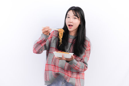 Indonesian woman wearing red checkered sweater enjoying fried noodlesの写真素材