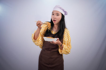 Indonesian woman in chef's uniform enjoying noodlesの写真素材