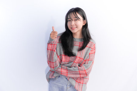 Asian woman wearing red checkered sweater smiling and giving thumbs up signの写真素材