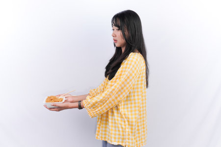 Indonesian Asian woman wearing yellow checkered shirt smiling and showing noodles in a containerの写真素材