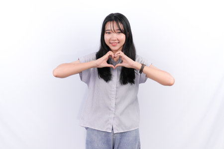 Indonesian Asian woman wearing white striped shirt smiling and giving love signの写真素材