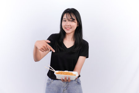 Indonesian Asian woman wearing black top smiling and showing noodles in a containerの写真素材
