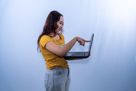 Indonesian Asian woman in yellow dress smiling and using laptopの写真素材