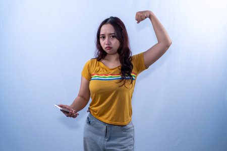 Indonesian Asian woman in yellow shirt holding smartphone and raising handsの写真素材