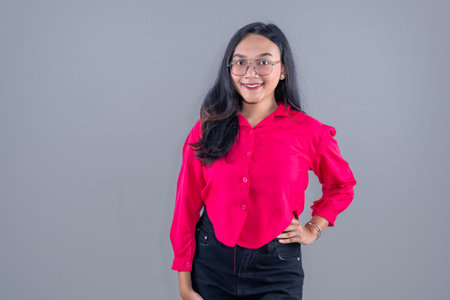 Asian woman in red blouse wearing glasses smiling and putting her hands on her hipsの写真素材