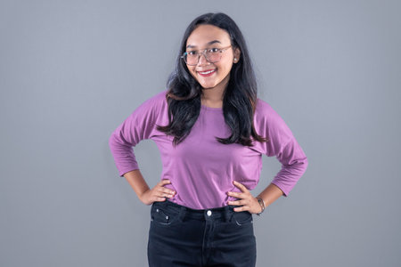 Asian woman in purple dress wearing glasses smiling and putting her hands on her hipsの写真素材