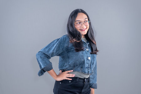 Asian Indonesian woman wearing jeans jacket with glasses smiling and hands on hipsの写真素材