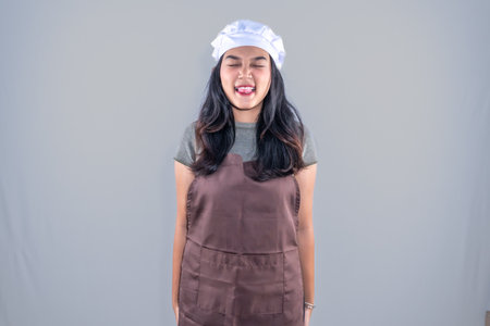 Asian Indonesian woman wearing cooking clothes closing one eye and opening her mouthの写真素材