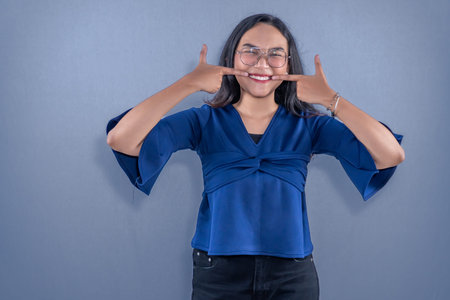 Indonesian Asian woman wearing blue dress smiling and pointing to her teeth