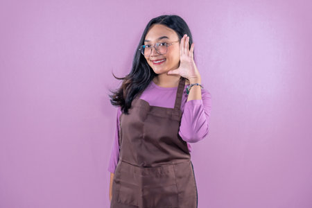 Indonesian Asian woman wearing brown cooking apron smiling and signaling listeningの写真素材