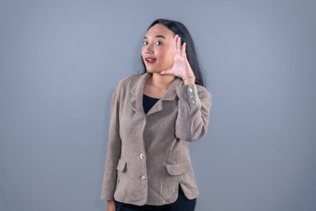 Indonesian Asian woman wearing a brown suit smiling and giving a whisper signal