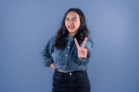 Indonesian Asian woman wearing blue jean jacket giving peace signの写真素材