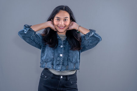 Indonesian Asian woman wearing blue jean jacket smiling and holding neckの写真素材