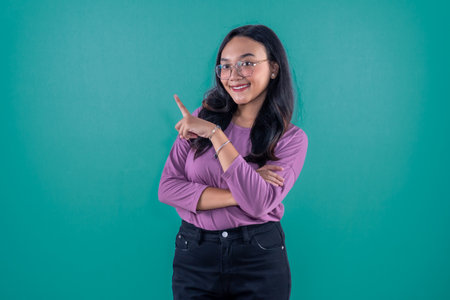 Indonesian Asian woman wearing purple clothes smiling and pointing to the sideの写真素材