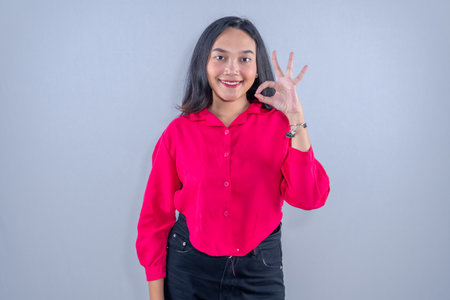Indonesian Asian woman wearing pink blouse and black pants smiling and giving ok signの写真素材