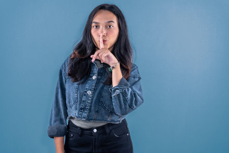 Indonesian Asian woman wearing blue jeans jacket signaling for silence