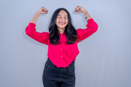 Asian Indonesian woman wearing red blouse and black pants smiling and raising both handsの写真素材
