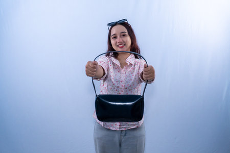 Indonesian Asian woman wearing white floral patterned dress smiling and showing black bagの写真素材