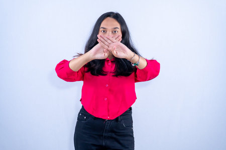 A woman in a red shirt stands with her hands crossed in front of her mouth, signaling silence or...