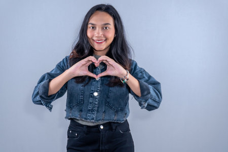 Indonesian Asian woman wearing blue jeans jacket smiling and making heart signの写真素材