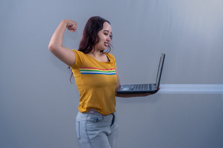 Asian Indonesian woman wearing yellow shirt operating laptopの写真素材