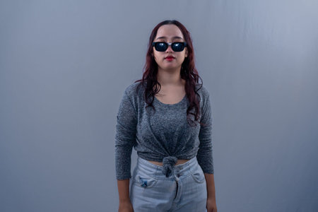 Asian Indonesian woman wearing grey shirt and sunglasses standing straight