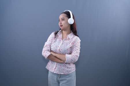 A young woman wearing a floral blouse and light jeans stands with her arms crossed, listening to...