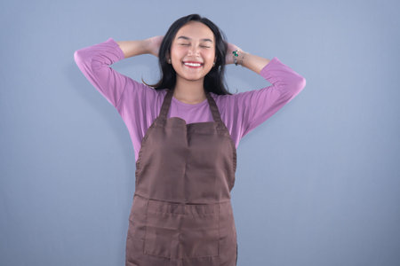 A woman with her hands behind her head and eyes closed smiling in a purple shirt