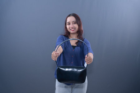 A young woman in blue top and jeans, pulling a black handbag, smiling in profileの写真素材