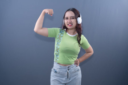 A young Asian woman in a green top and headphones, flexing arm with a strained expression