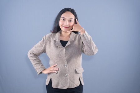 A smiling young woman in a blazer making a call me gesture with her left hand.の写真素材