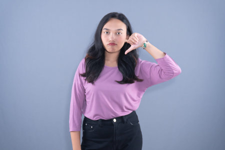 A young woman in a purple shirt giving a thumbs-down gesture, looking disappointed.