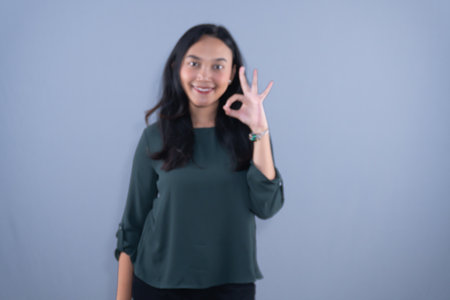 A smiling young woman in a green shirt is making an OK gesture with her left hand.の写真素材