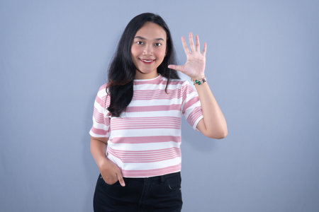 A smiling young woman in a striped shirt holding her hand up with five fingers extended.の写真素材