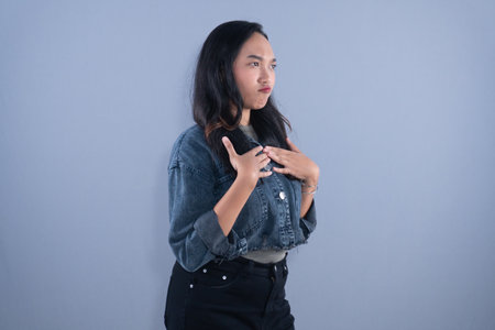 A young woman in a denim jacket with a concerned expression, hands on her chest, looking to the side.の写真素材