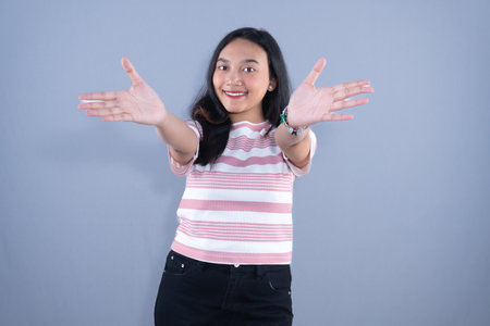 A smiling young woman with dark hair, wearing a striped shirt, holding her arms out wide.の写真素材