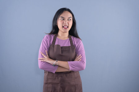 A woman in a purple shirt and brown apron crosses her arms, looking away.の写真素材