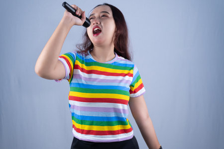 A woman sings into a microphone, wearing a colorful striped t-shirt. She has her eyes closed.の写真素材