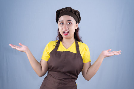 A woman in a chef's apron and hat gestures with open palms and a surprised expression.の写真素材