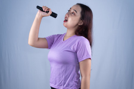 A woman in a purple shirt sings into a microphone with an open mouth and tilted head.の写真素材