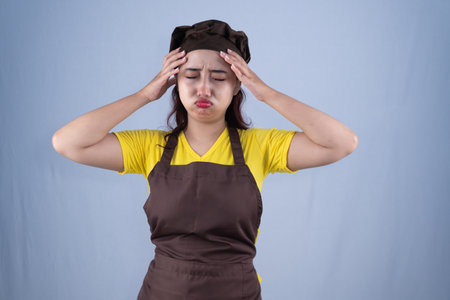 A woman in a chef's apron and hat, with her hands on her head.の写真素材