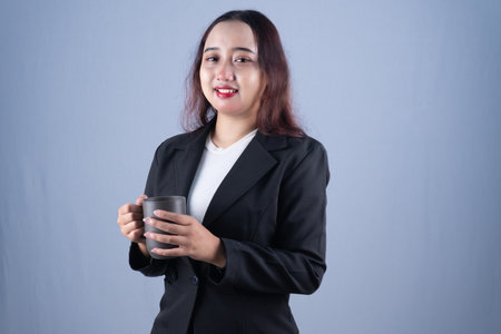 A smiling woman in a black blazer holds a gray mug, looking at the camera.の写真素材