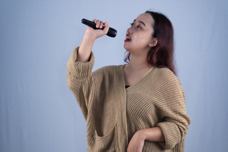 A woman in a brown sweater sings into a microphone with her eyes slightly closed.の写真素材